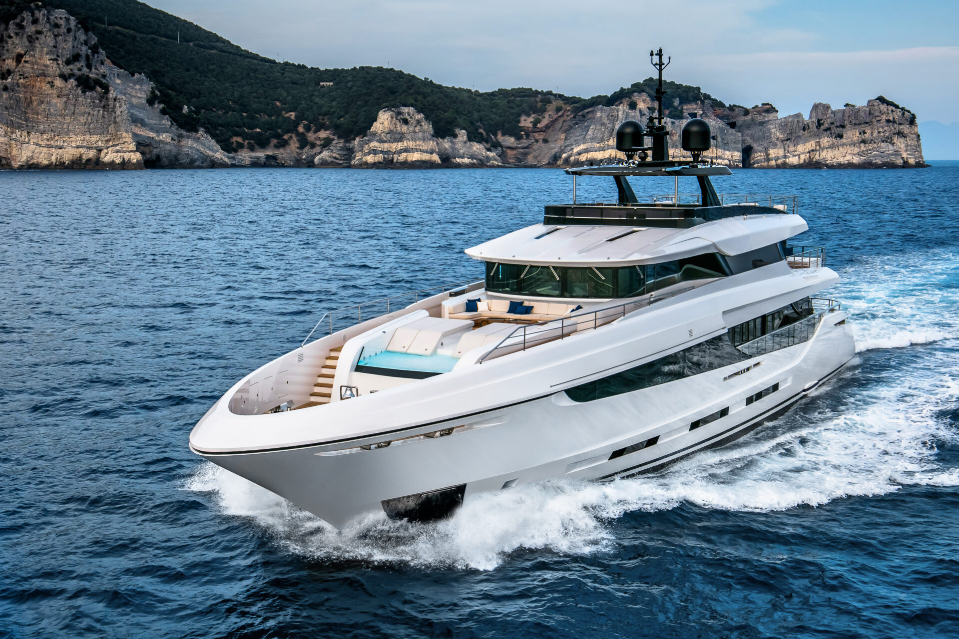 Mangusta yacht cruising near rocky coastline.
