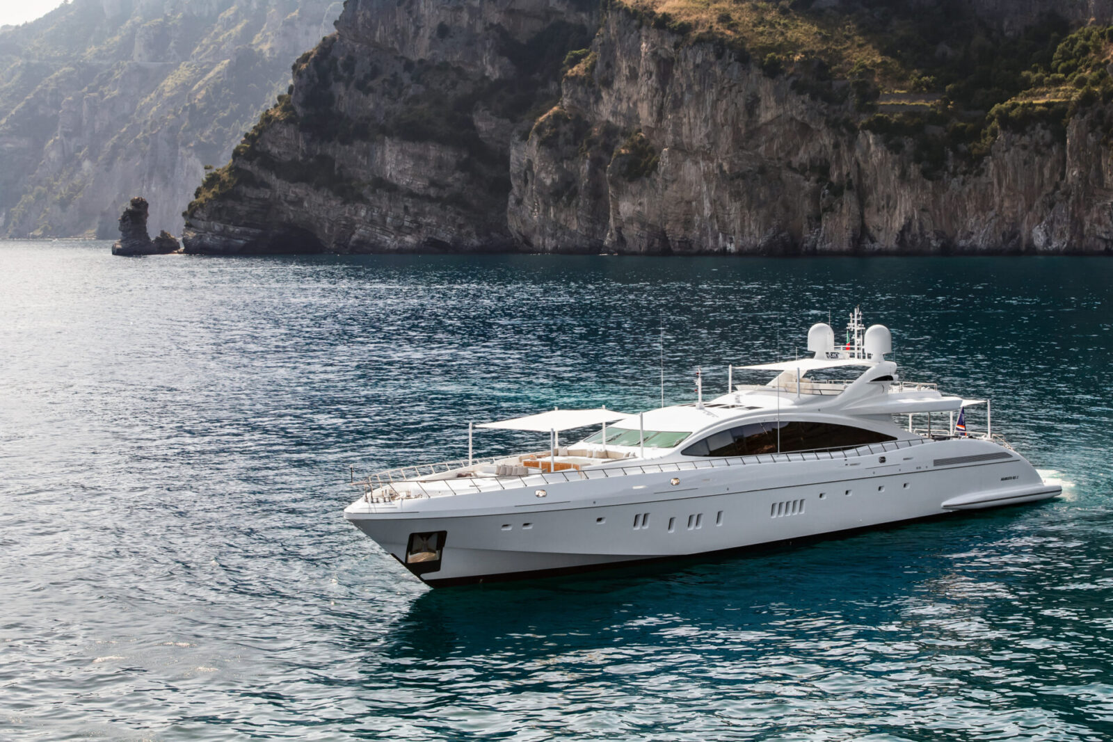 Yacht Mangusta naviga vicino a riva rocciosa.