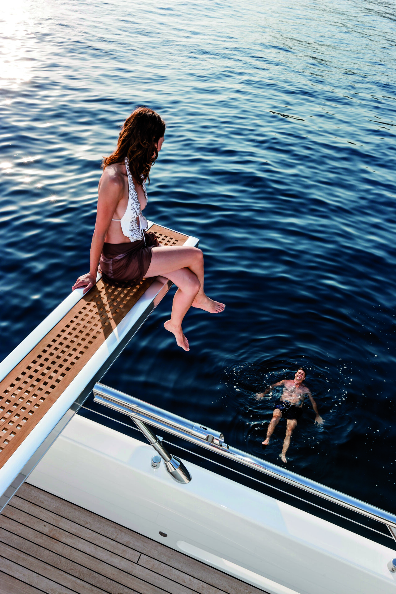 Woman relaxing on Mangusta yacht deck, man swimming.