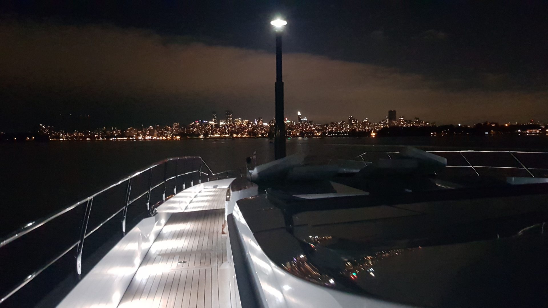 Yacht Mangusta di notte con skyline illuminato.