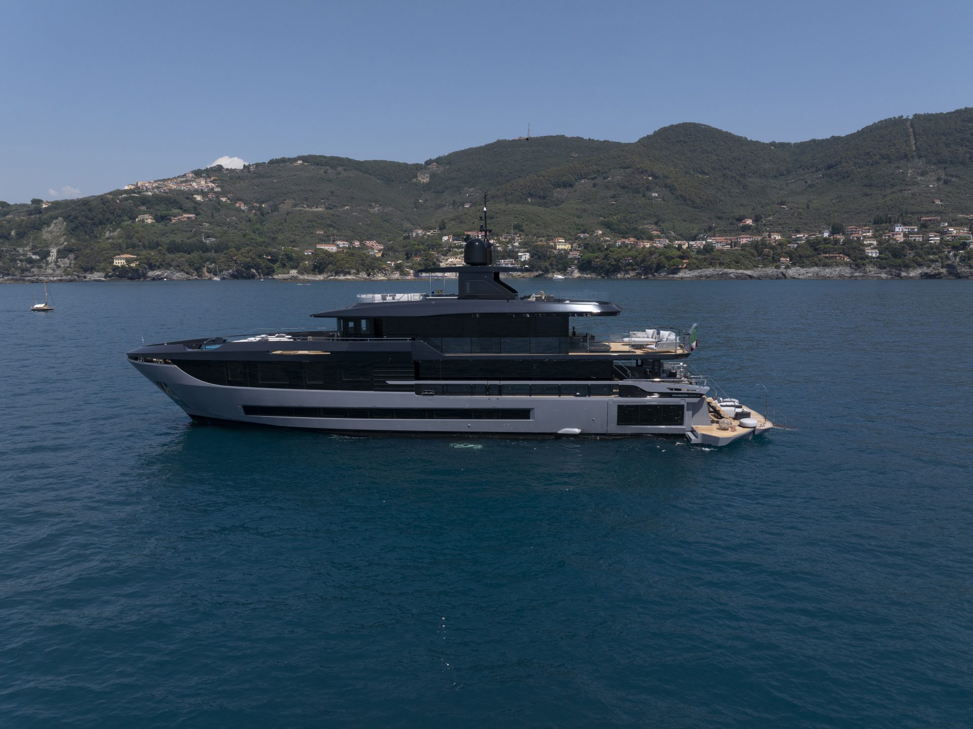 Luxurious Mangusta yacht near coastal mountains.